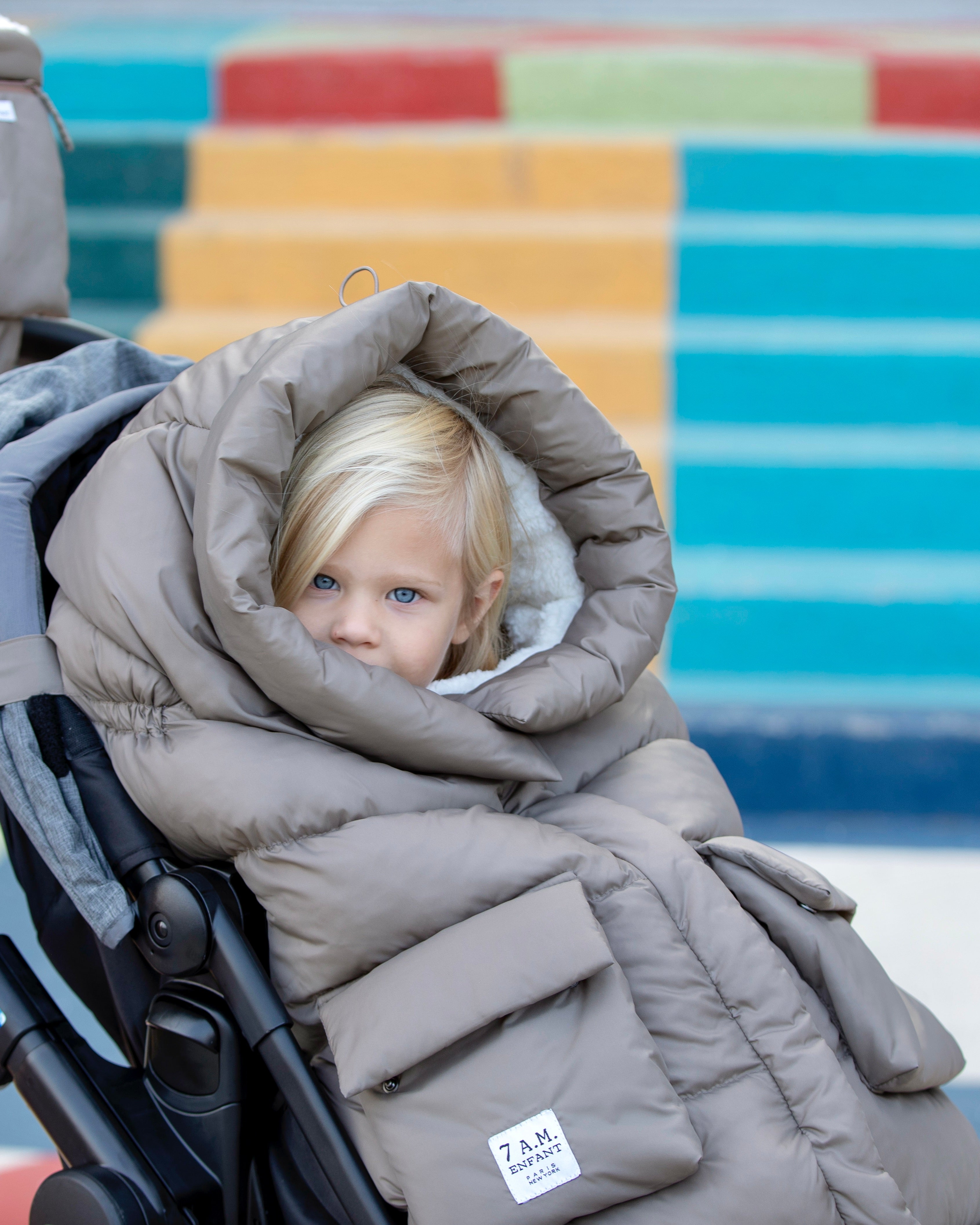 a blond child in a stroller inside a footmuff